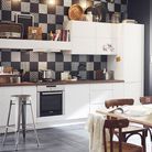 Une cuisine aux meubles blancs associés à une crédence et des murs noirs 